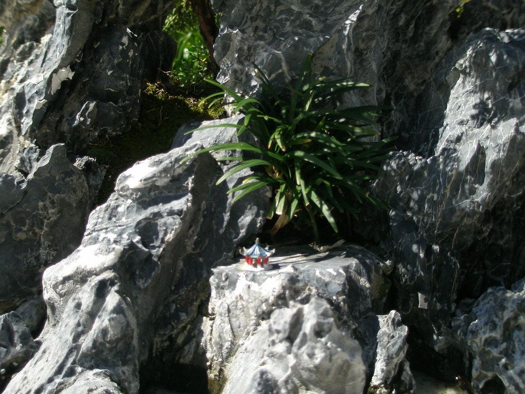 灰色の岩を重ねた山水盆景。岩の上に小さな塔の添え物が置かれ、草が植えられている
